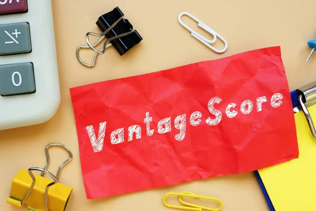 A red, crumpled paper with the word VantageScore written on it lies on a desk surrounded by binder clips, paper clips, part of a calculator, and a yellow notebook.