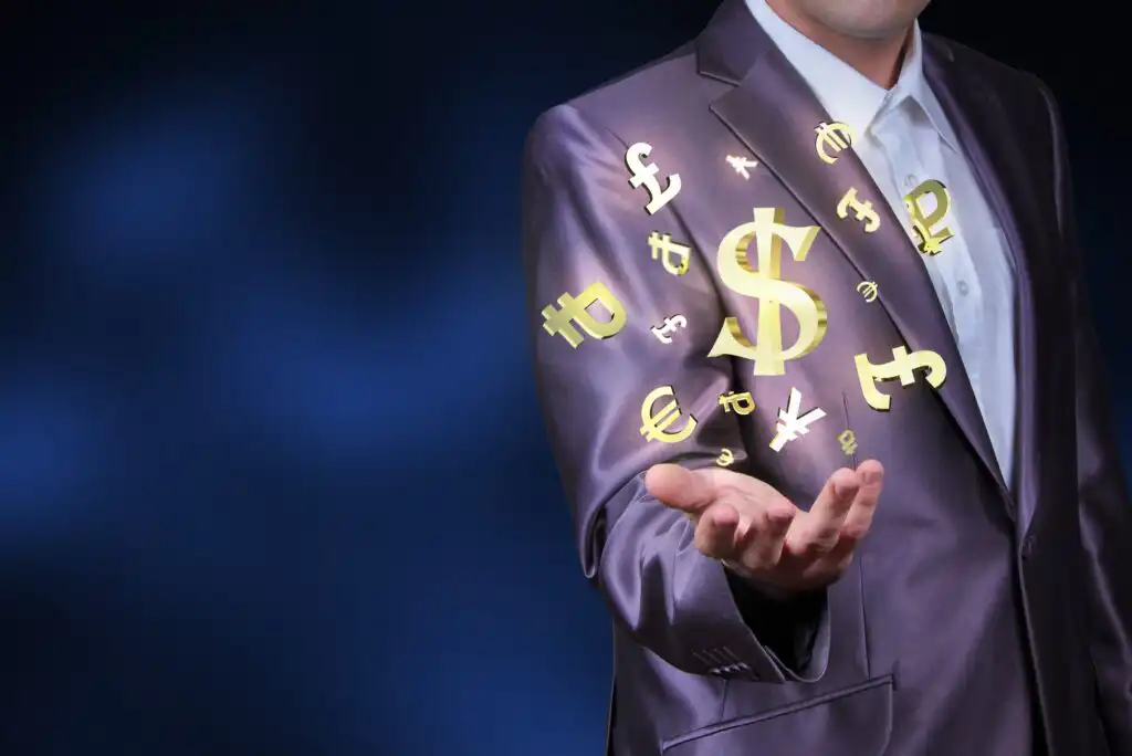 A man in a suit holds out his hand as golden currency symbols, including the dollar, euro, and yen, float above his palm against a dark blue background.
